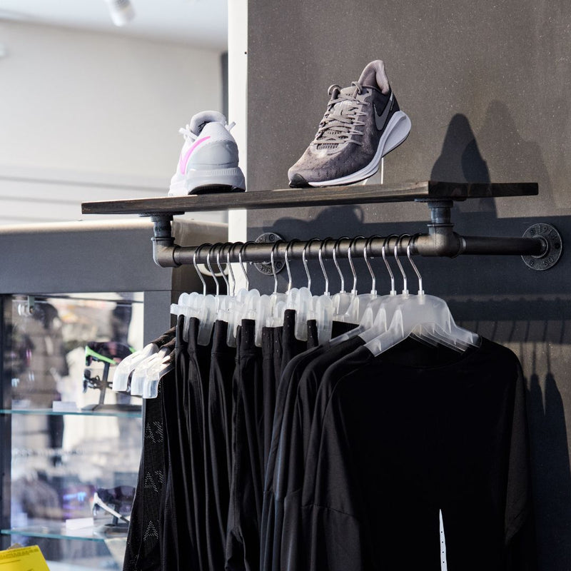 Dunkle Eisenrohre und dunkle Kiefer Wandmontiertes Regal mit Kleiderstange im Bekleidungsgeschäft als Präsentationsfläche