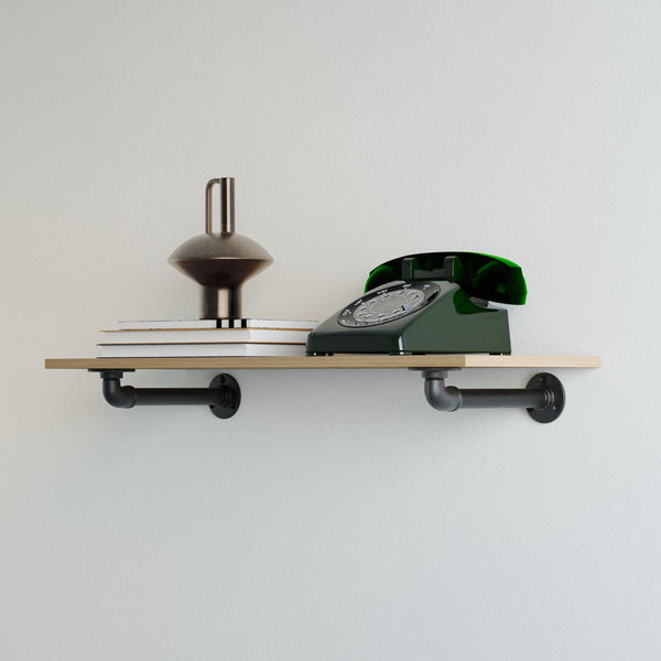 Helles Wandregal mit schwarzen Rohrhalterungen, darauf ein grünes Wählscheibentelefon, ein metallisches Dekoobjekt und gestapelte Bücher