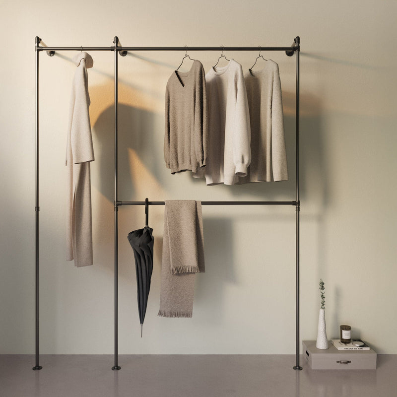 Schlichter Kleiderständer mit beigen Pullovern, Schal, Regenschirm und kleinen Dekorationen vor hellem Hintergrund