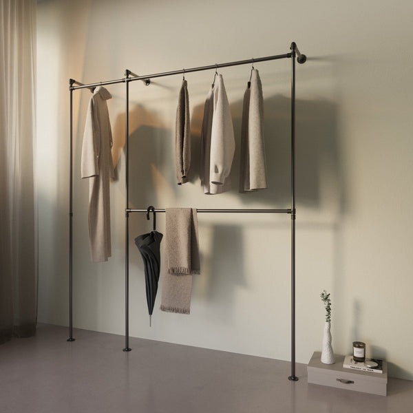 Minimalistische Kleiderstange mit neutralen Kleidungsstücken, Schirm und Deko vor hellgrünem Hintergrund in schlichtem Raum